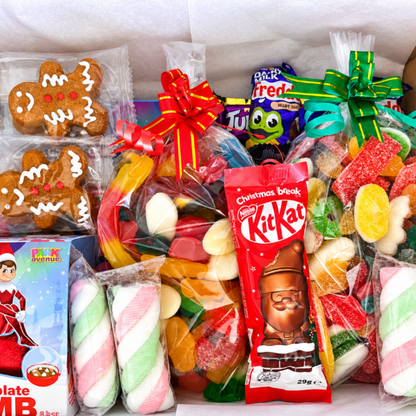 A gift box filled with assorted candies, gummy marshmallows, gingerbread cookies, chocolate bars, and sweets, arranged together in a hamper with tissue paper lining.